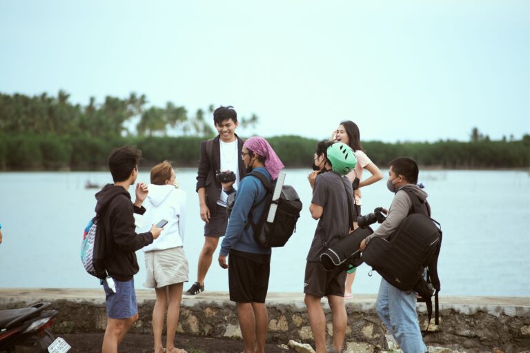 A group of young adults laughing and hanging out by a serene lakeside.