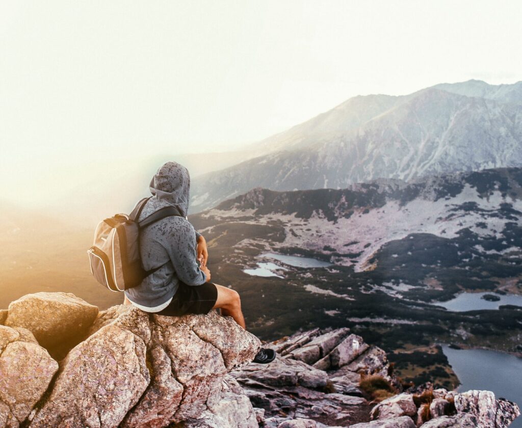 A lone traveler with a backpack sitting on a mountain rock, enjoying the scenic sunrise view.