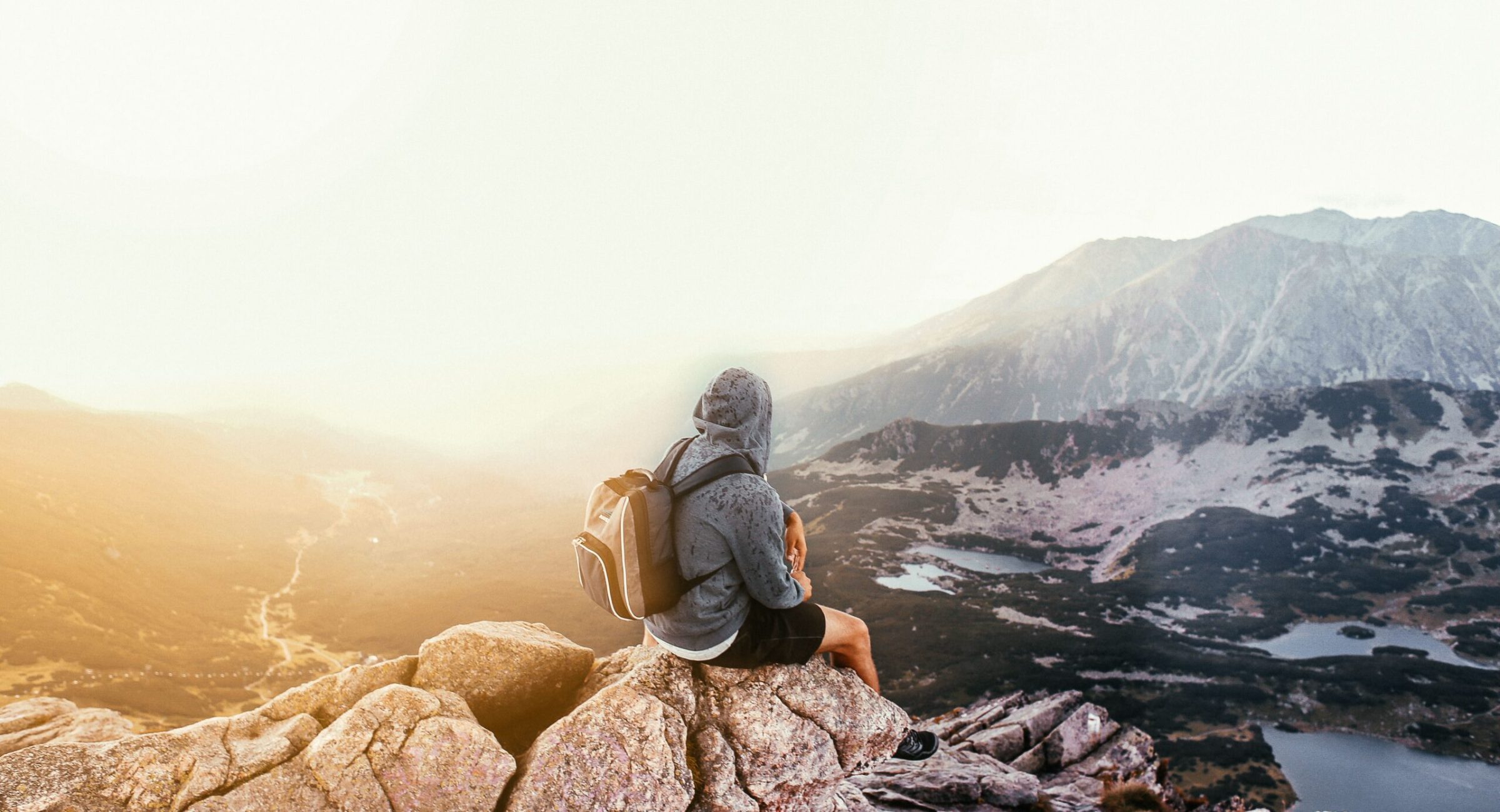 A lone traveler with a backpack sitting on a mountain rock, enjoying the scenic sunrise view.